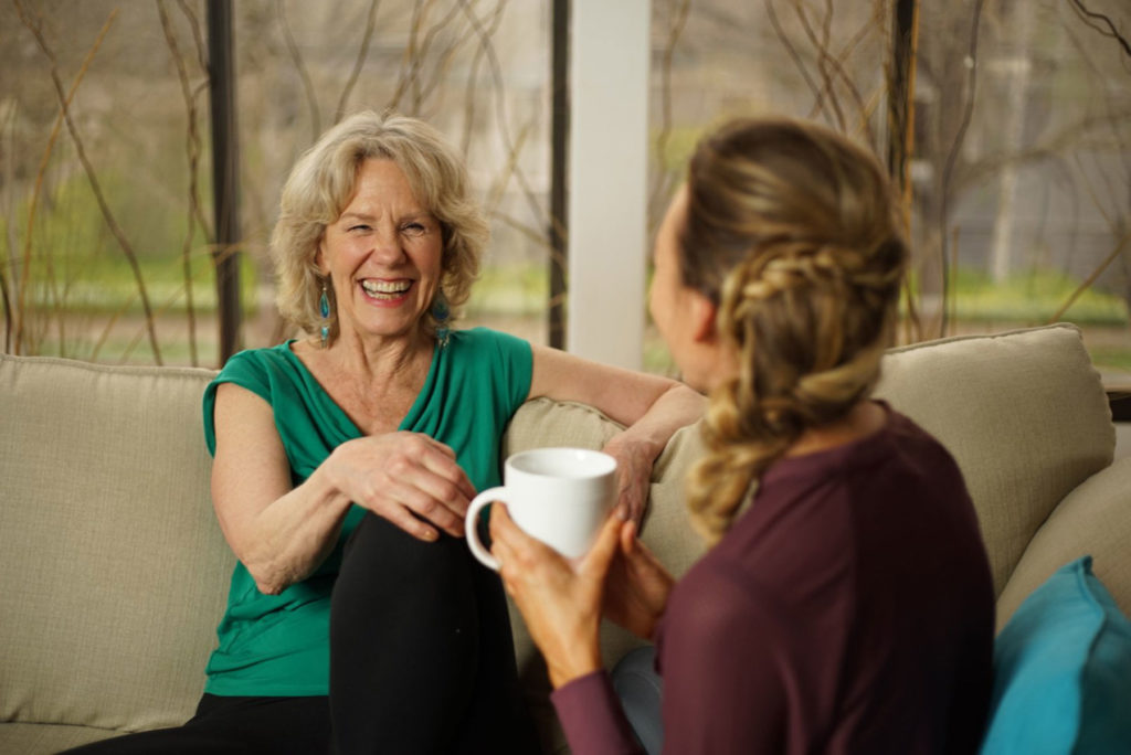 two women laughing while sitting on couch