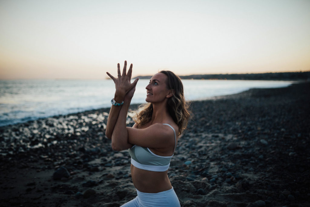A woman dressed in white doing a yoga pose with her hands on the beach