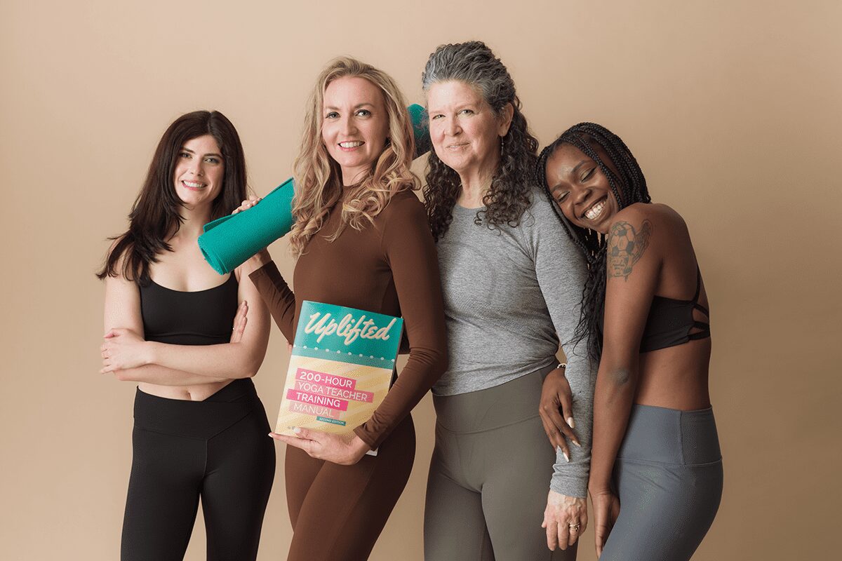 Brett Larkin posing with a group of women. She is holding a yoga mat in one hand and the 200-hour Uplifted Yoga Teacher Training manual in the other.