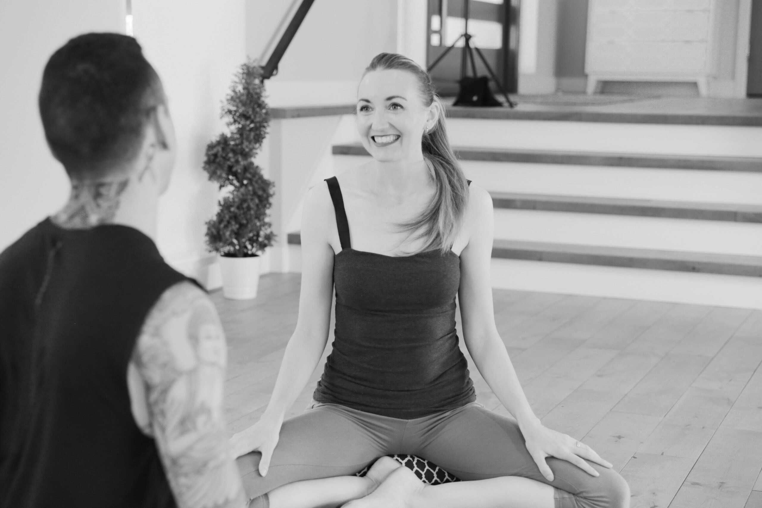 Brett Larkin smiling and sitting on a yoga bolster while yoga life coaching a yoga student