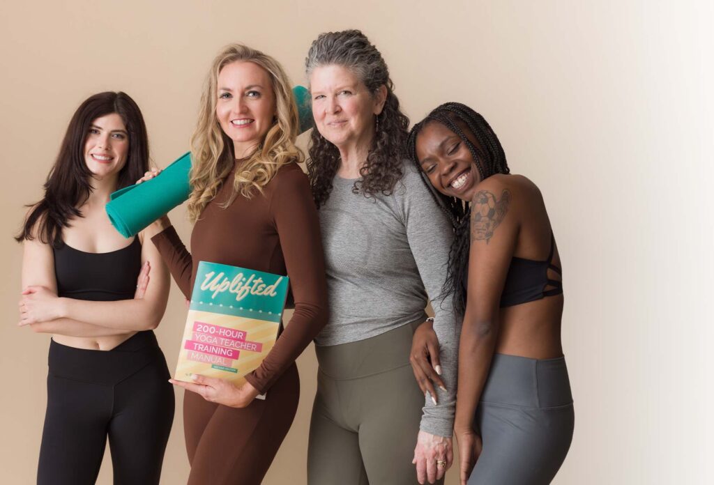 Brett Larkin posing with a group of women. She is holding a yoga mat in one hand and the 200-hour Uplifted Yoga Teacher Training manual in the other.